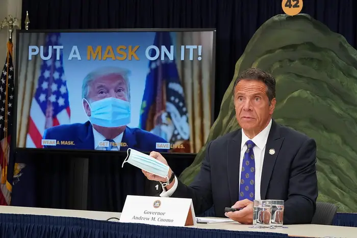 Governor Andrew Cuomo at a press briefing in front of a photo of President Trump in a Photoshopped mask with the words "Put A Mask On It!" in July, 2020.